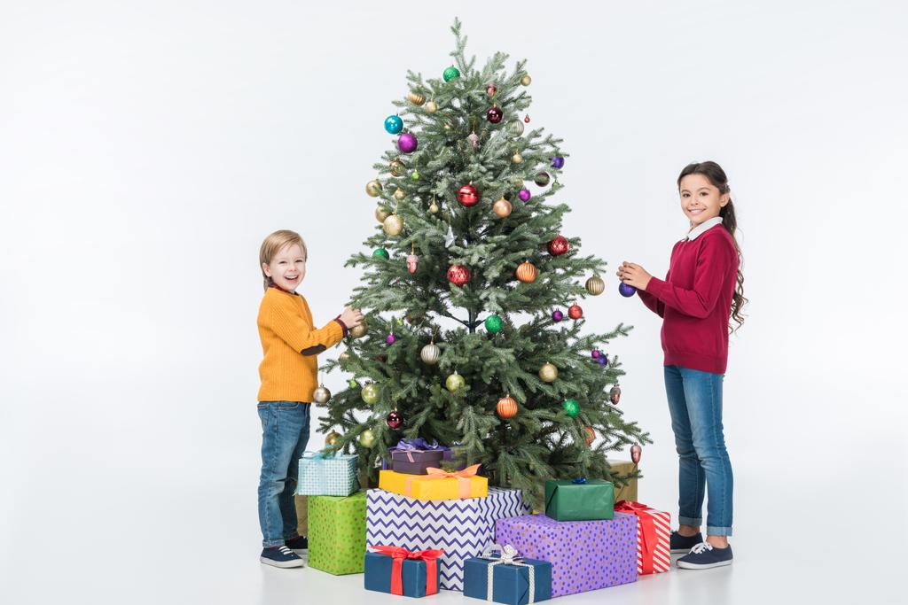 sonrientes hermanos decorando árbol de navidad con regalos aislados en blanco
 - Foto, imagen