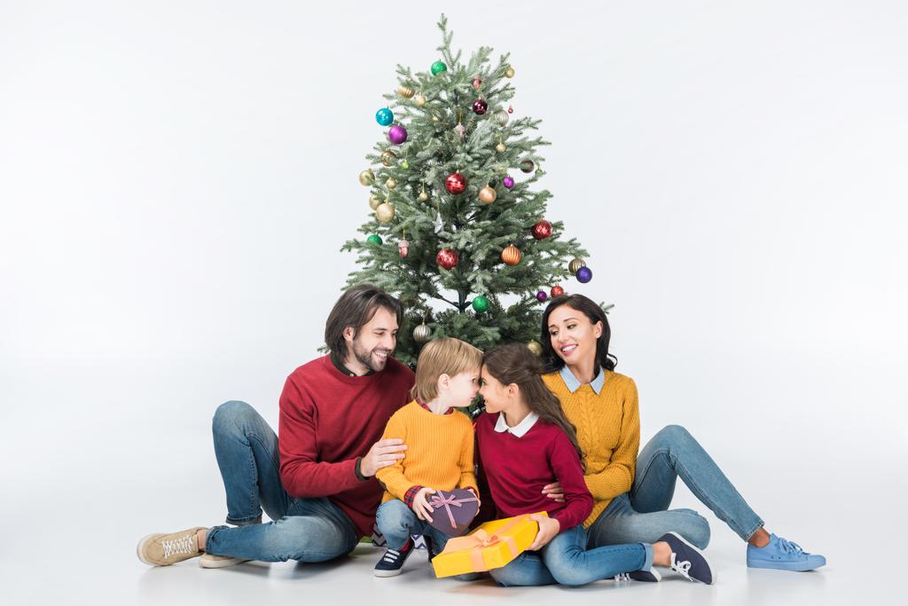 Bambini felici con regali con i genitori seduti vicino all'albero di Natale isolato su bianco
 - Foto, immagini