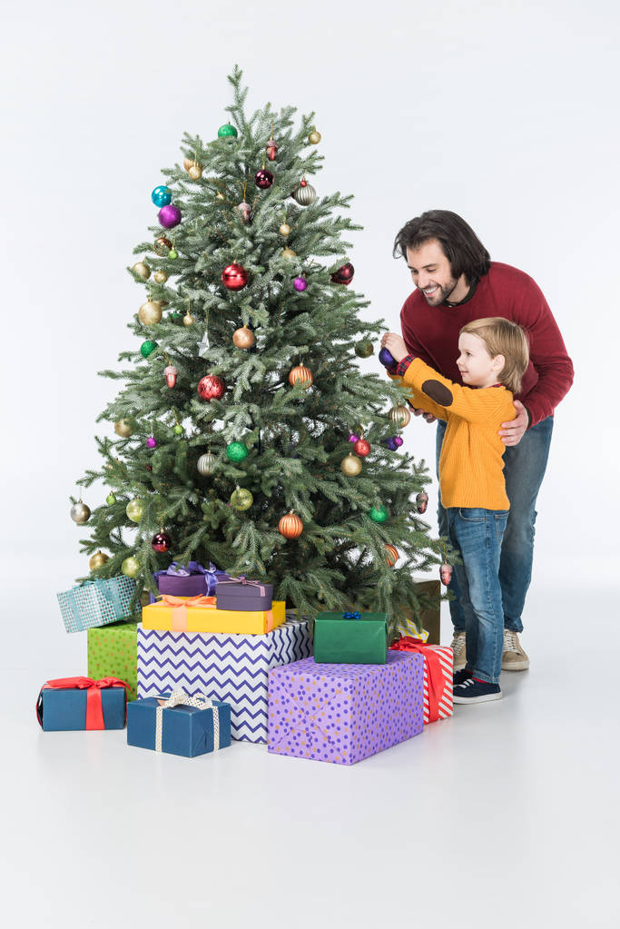 усміхнений батько з сином прикрашає ялинку подарунками ізольовано на білому
 - Фото, зображення