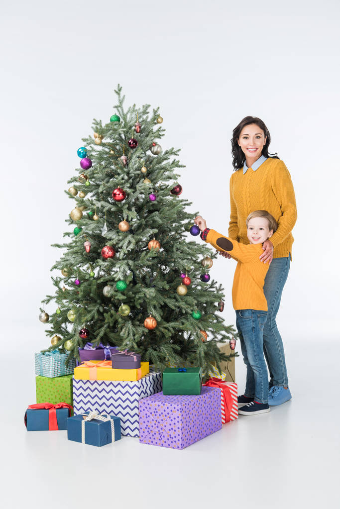 Lächelnde Mutter mit Sohn schmückt Weihnachtsbaum mit Geschenken auf Weiß - Foto, Bild