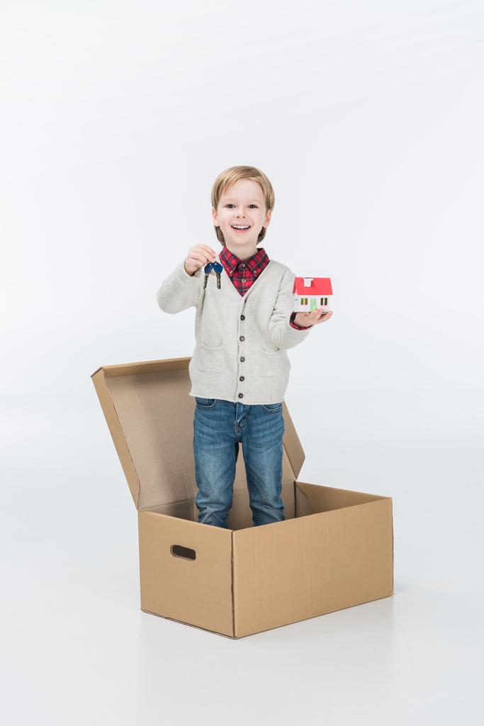Маленький мальчик держит картонный домик и ключ от нового дома, готовый переехать в новый дом изолированный на белом
  - Фото, изображение