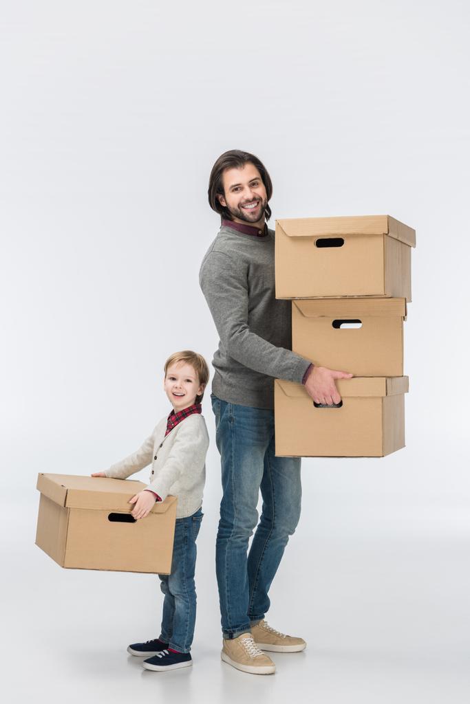 otec drží stack lepenkových krabic a syn mu izolované na bílém - Fotografie, Obrázek