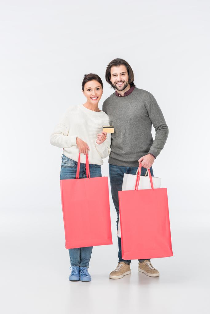 casal sorrindo com sacos de compras e mulher mostrando cartão de crédito isolado no branco
  - Foto, Imagem