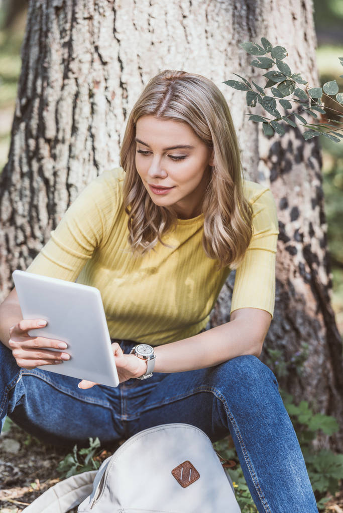 Porträt einer jungen Frau, die während ihrer Ruhepause im Park ein digitales Tablet benutzt - Foto, Bild