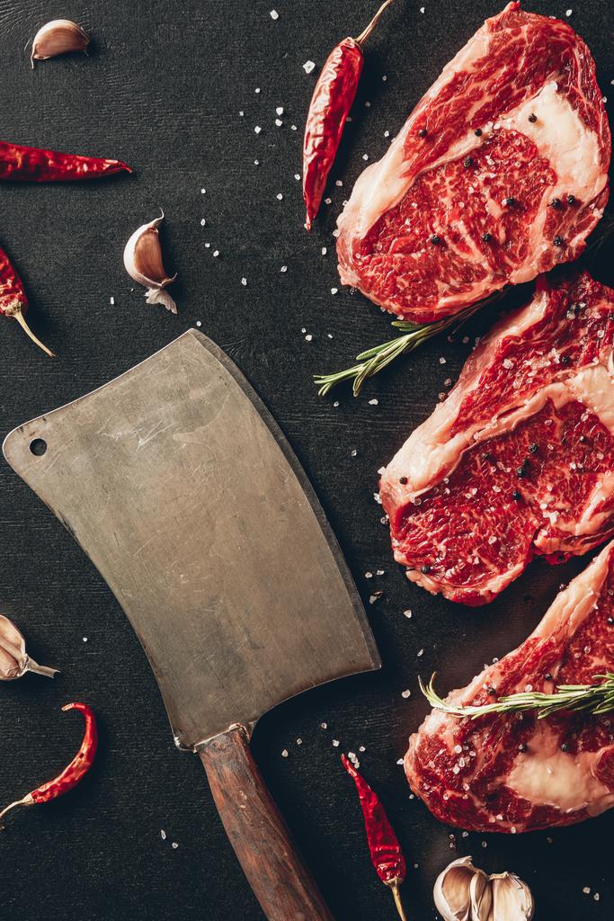 vue de dessus des steaks de viande crue, des épices et du fendoir sur la surface dans la cuisine
  - Photo, image