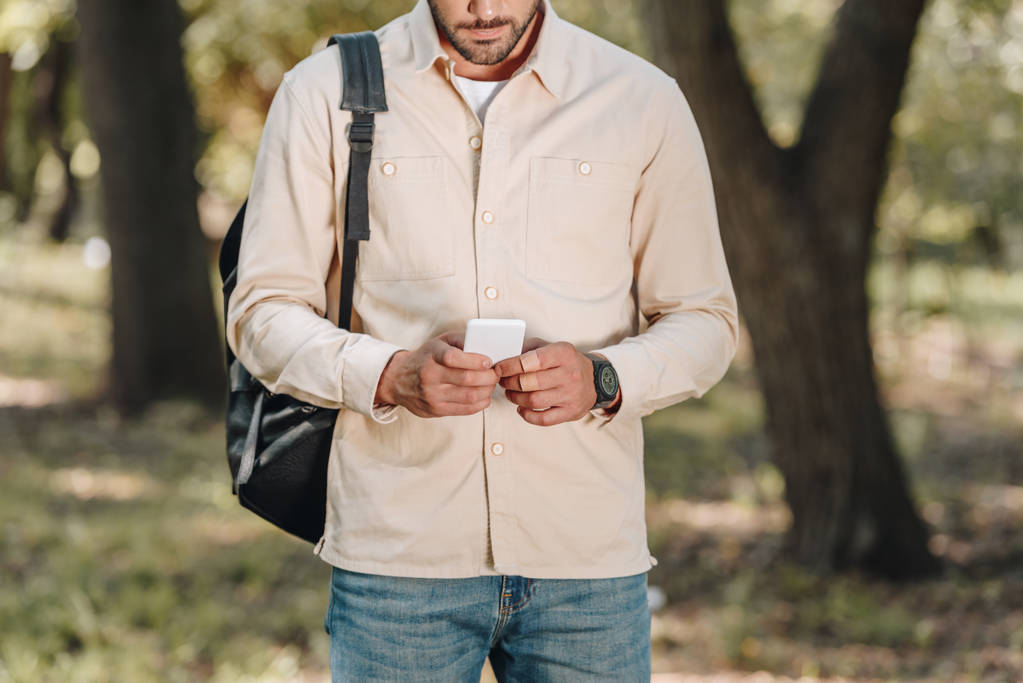 vue partielle de l'homme en vêtements décontractés avec sac à dos en utilisant smartphone dans le parc
 - Photo, image
