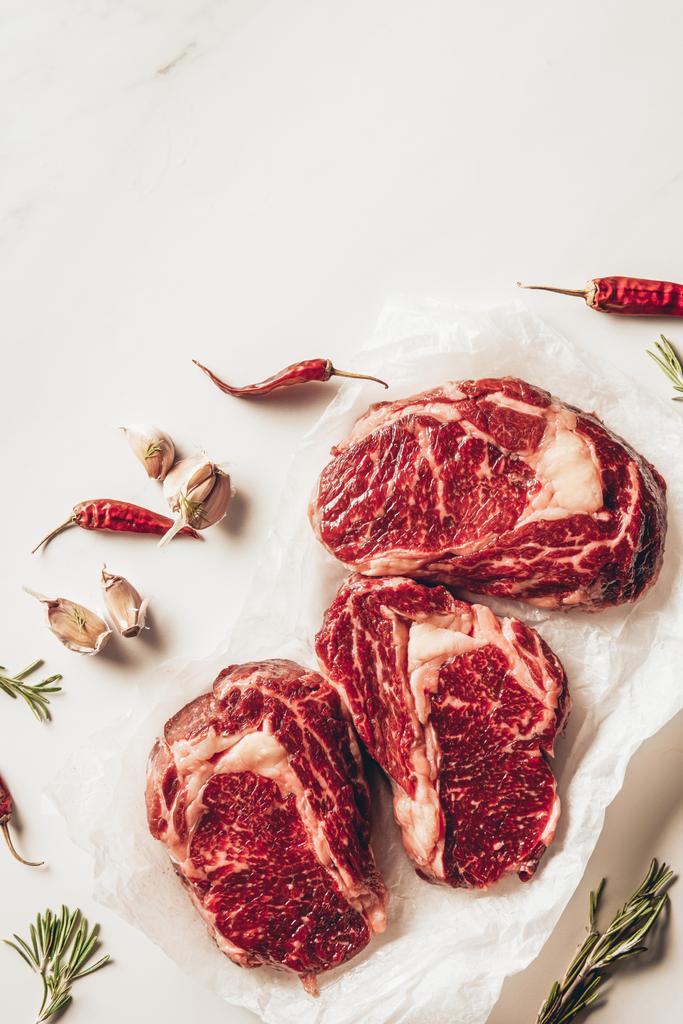 bovenaanzicht van drie stukken van rauw vlees steaks en groenten op bakken papier in keuken - Foto, afbeelding