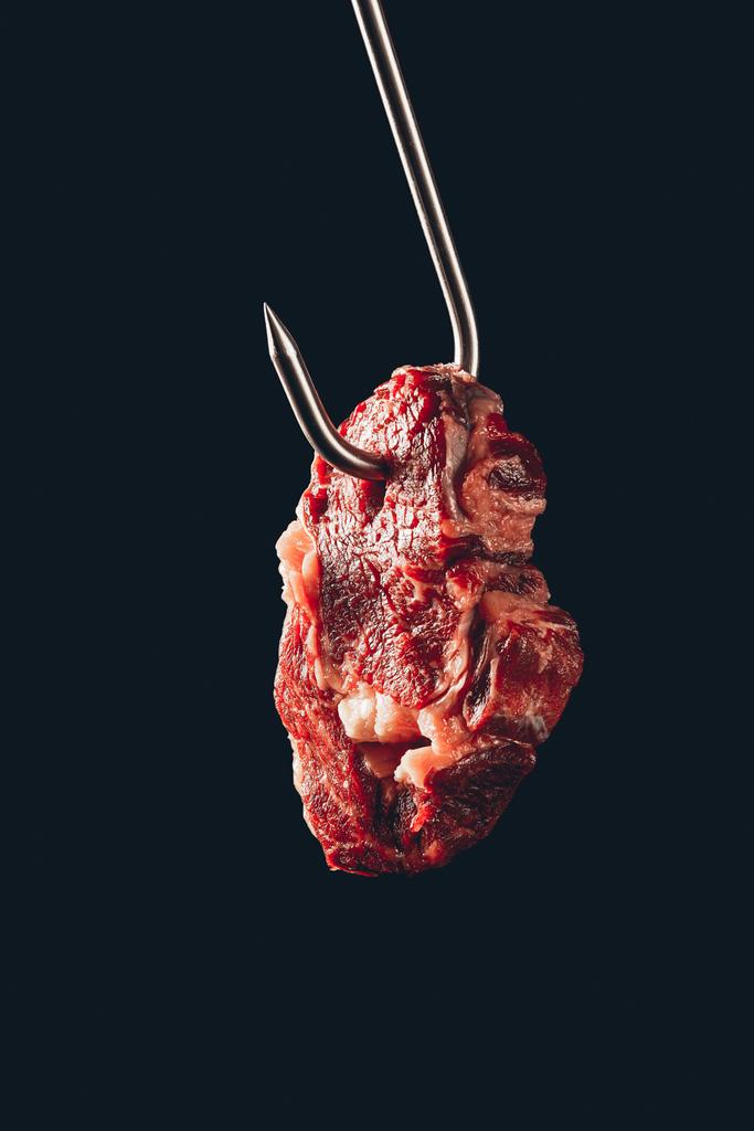 piece of raw meat hanging on metal hook isolated on black - Photo, Image