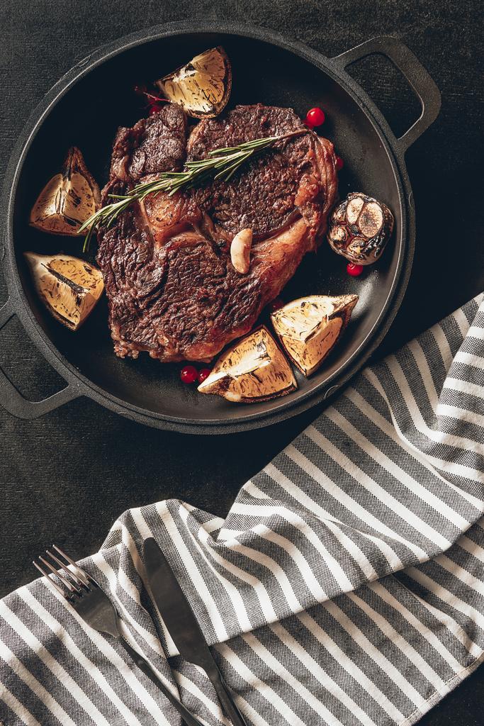 elevated view of cooked steak with lemons and berries on frying pan, striped tablecloth on surface in kitchen - Photo, Image