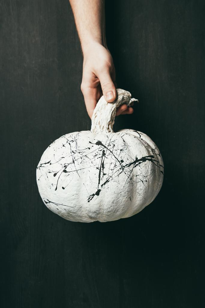 cropped view of person holding white pumpkin with black paint splatters in hand, halloween decoration  - Photo, Image