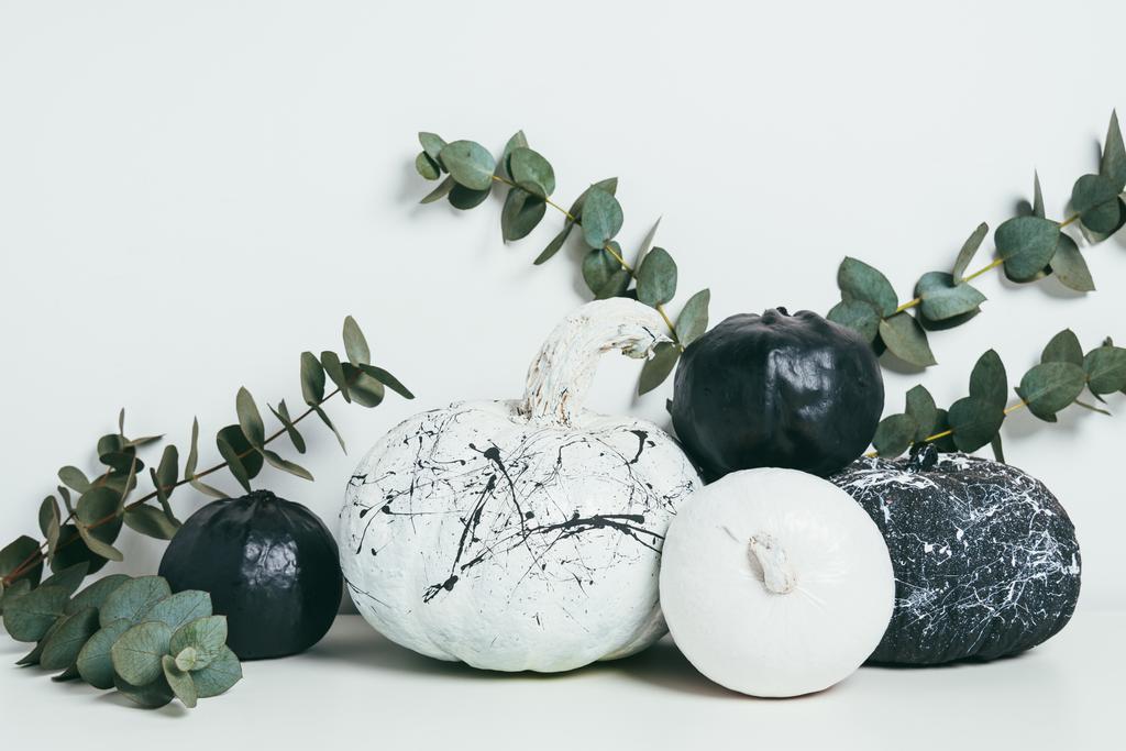 schwarz-weiße Kürbisse mit Farbspritzern und Eukalyptusblättern, herbstliche Dekoration - Foto, Bild