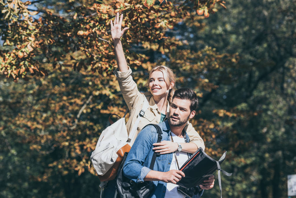 Portret van jonge vrolijke reizigers met kaart, meisje zwaaien in herfst park - Foto, afbeelding