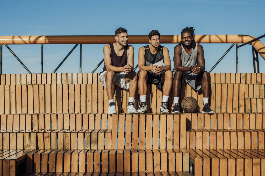 Багатоетнічна група невпізнаваних баскетболістів, які сидять біля двору і дивляться на камеру
. - Фото, зображення