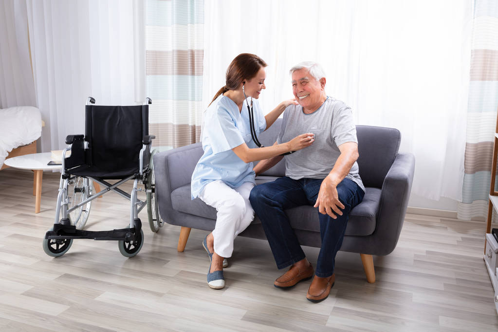 Enfermera revisando feliz hombre mayor sentado en un sofá con estetoscopio
 - Foto, imagen