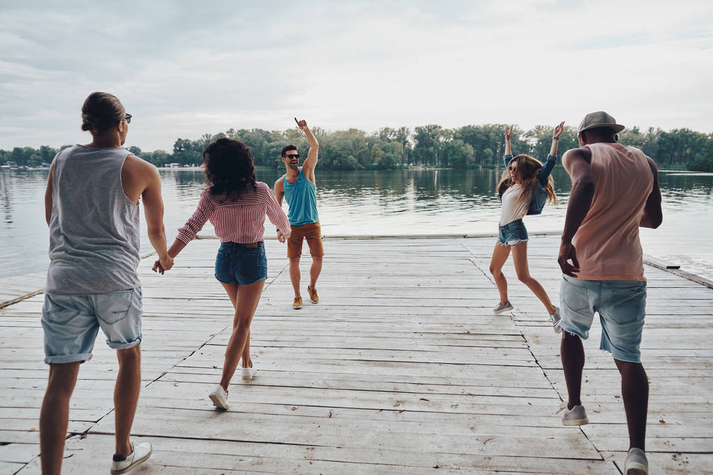 groep van gelukkige mensen in vrijetijdskleding uitgevoerd op houten pier bij lake  - Foto, afbeelding