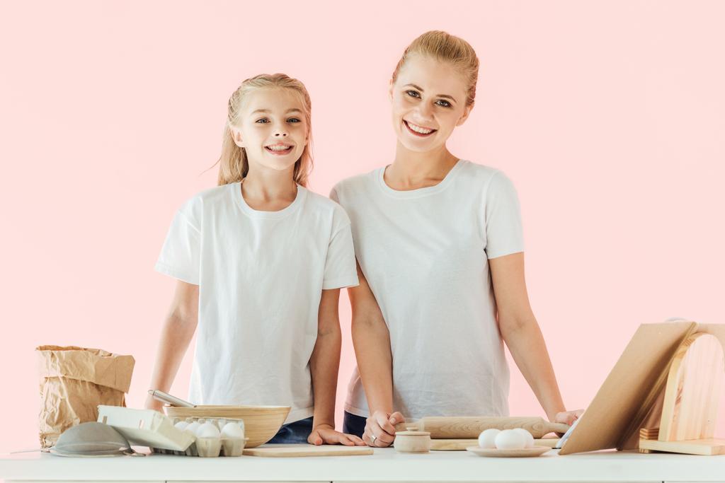 güzel anne ve kızı beyaz t-shirt birlikte yemek yaparken kameraya bakarak içinde pink izole - Fotoğraf, Görsel
