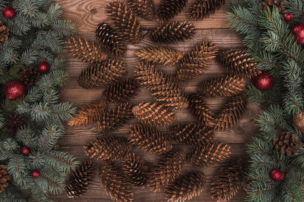 top view of brown pine cones with fir twigs and red baubles on wooden background  - Photo, Image