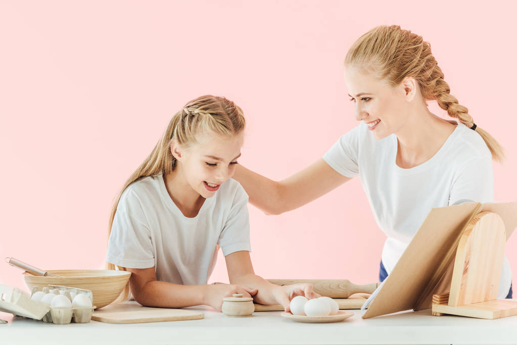 happy young mother and daughter in white t-shirts cooking together isolated on pink - Photo, Image