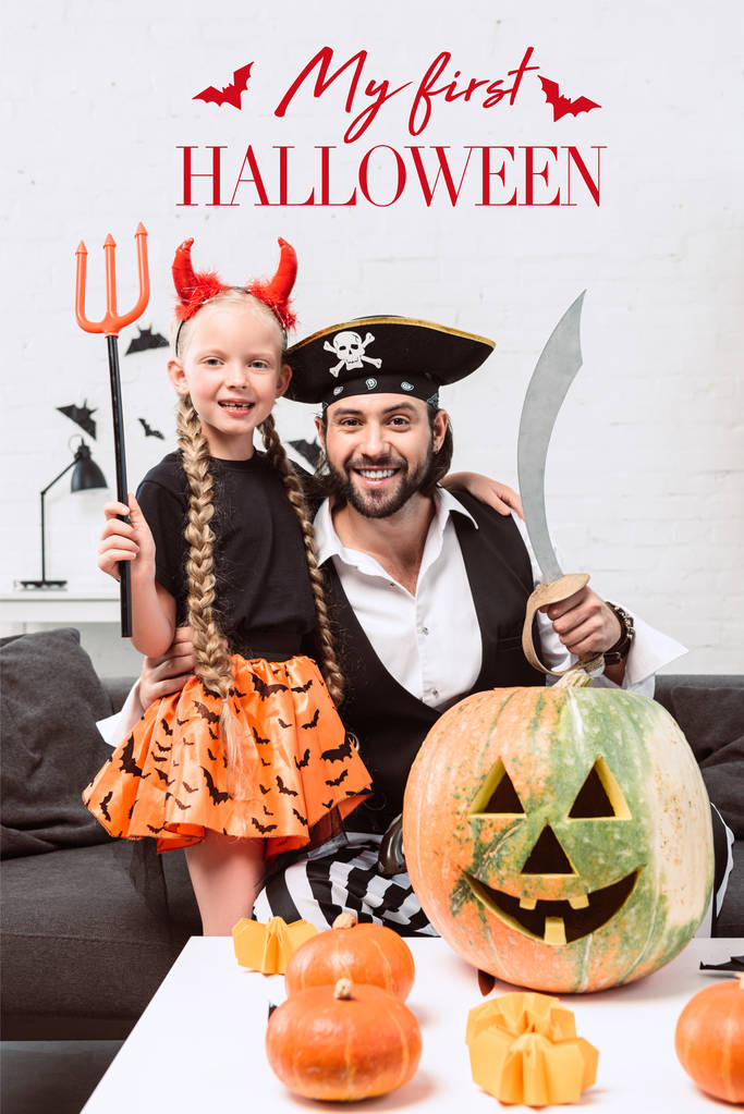 glückliche Tochter und Vater in Halloween-Kostümen zu Hause mit "meinem ersten halloween" Schriftzug  - Foto, Bild