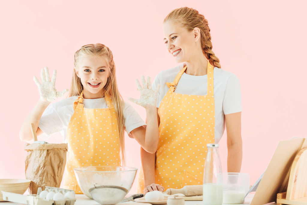 happy mother and daughter in yellow aprons cooking together isolated on pink - Photo, Image