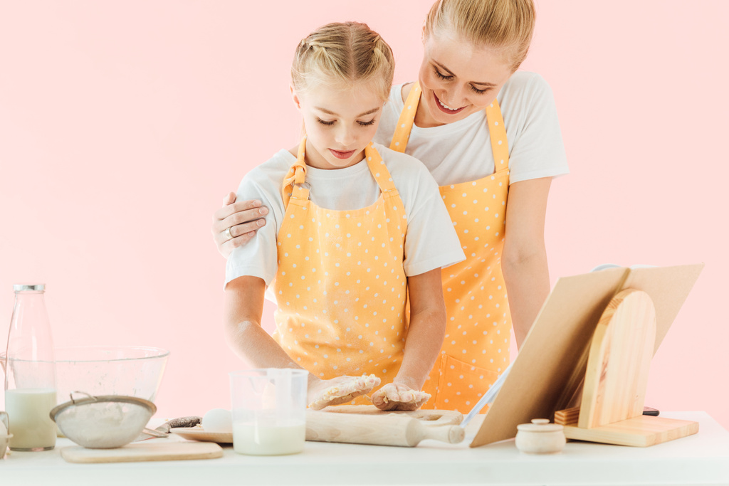 happy young mother and daughter cooking together isolated on pink - Photo, Image