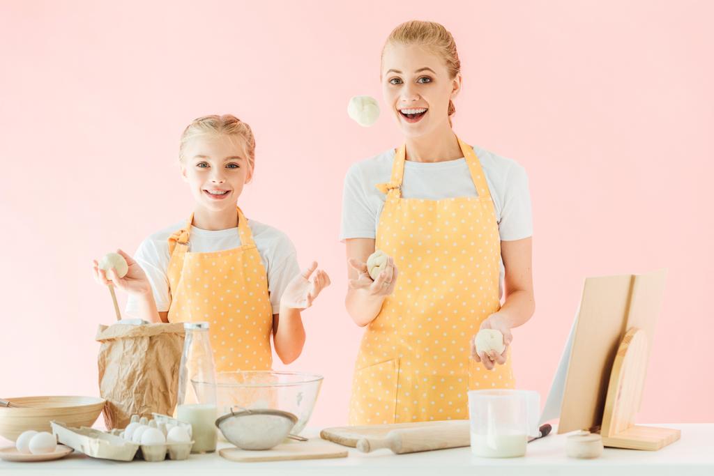 heureux mère et fille jongler avec des morceaux de pâte tout en cuisinant isolé sur rose
 - Photo, image