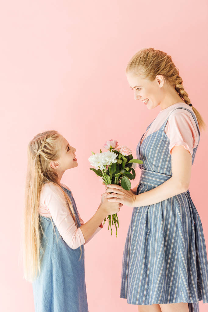 happy young mother and daughter holding beautiful bouquet and looking at each other isolated on pink - Photo, Image