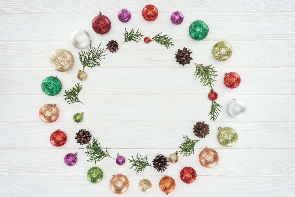 Blick von oben auf schön glänzende bunte Kugeln, Nadelzweige und Tannenzapfen auf Holzoberfläche, weihnachtlicher Hintergrund  - Foto, Bild