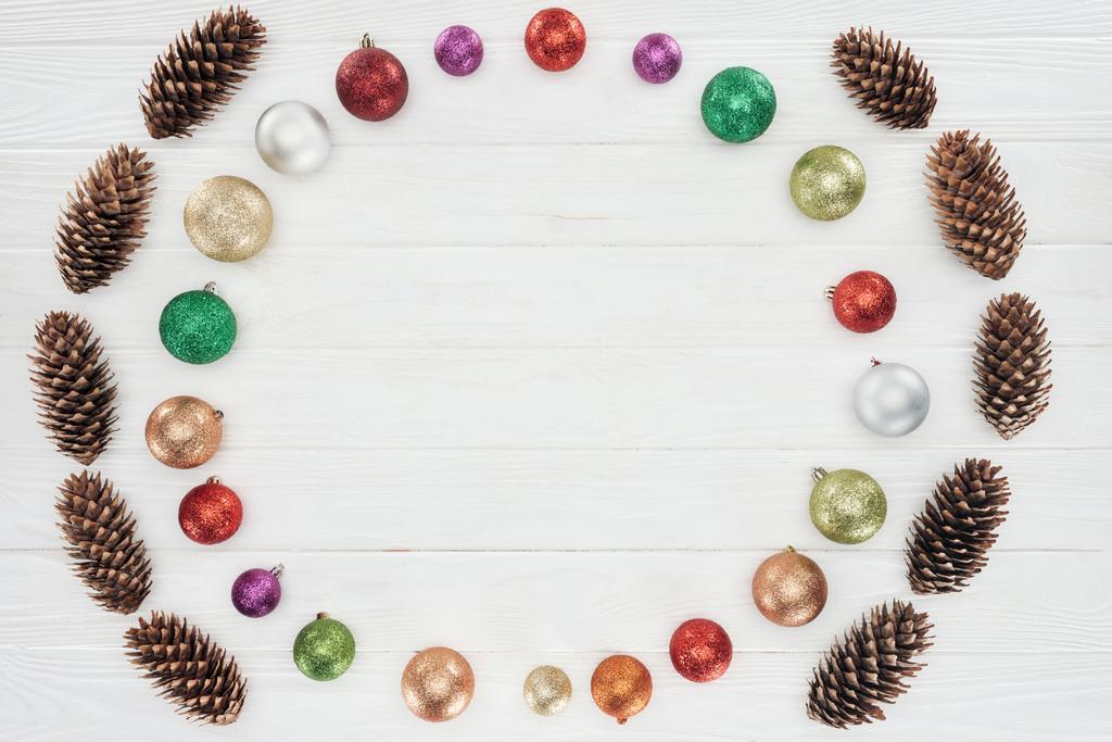 top view of beautiful shiny colorful baubles and pine cones on wooden surface, christmas background - Photo, Image