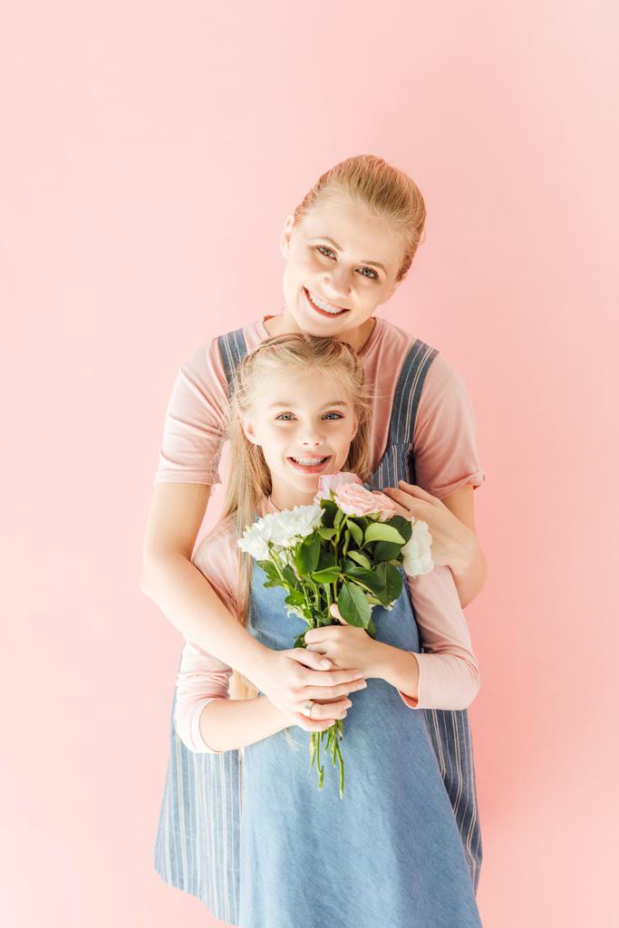 χαμογελώντας νεαρή μητέρα και κόρη του holding όμορφη ανθοδέσμη και βλέπουν τα φωτογραφικών μηχανών που απομονώνονται σε ροζ - Φωτογραφία, εικόνα