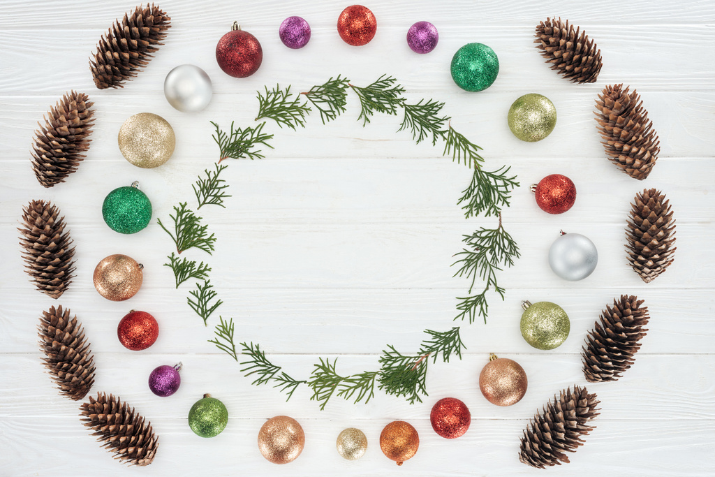 evergreen coniferous twigs, pine cones and shiny colorful baubles on white wooden background - Photo, Image