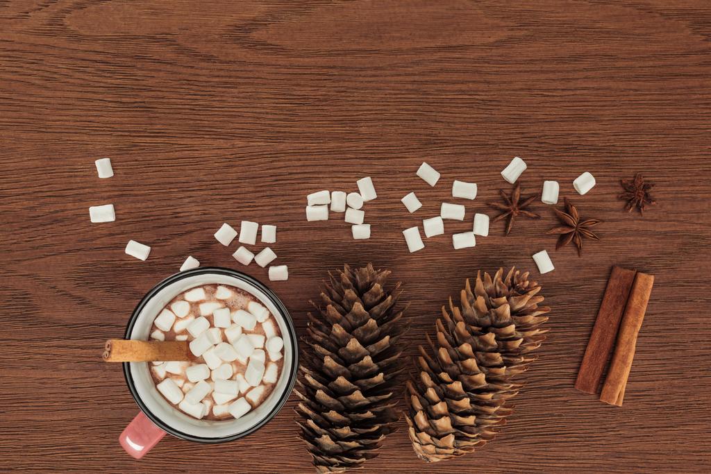 vista superior da xícara com chocolate quente, marshmallows, cones de pinho e paus de canela na mesa de madeira
 - Foto, Imagem