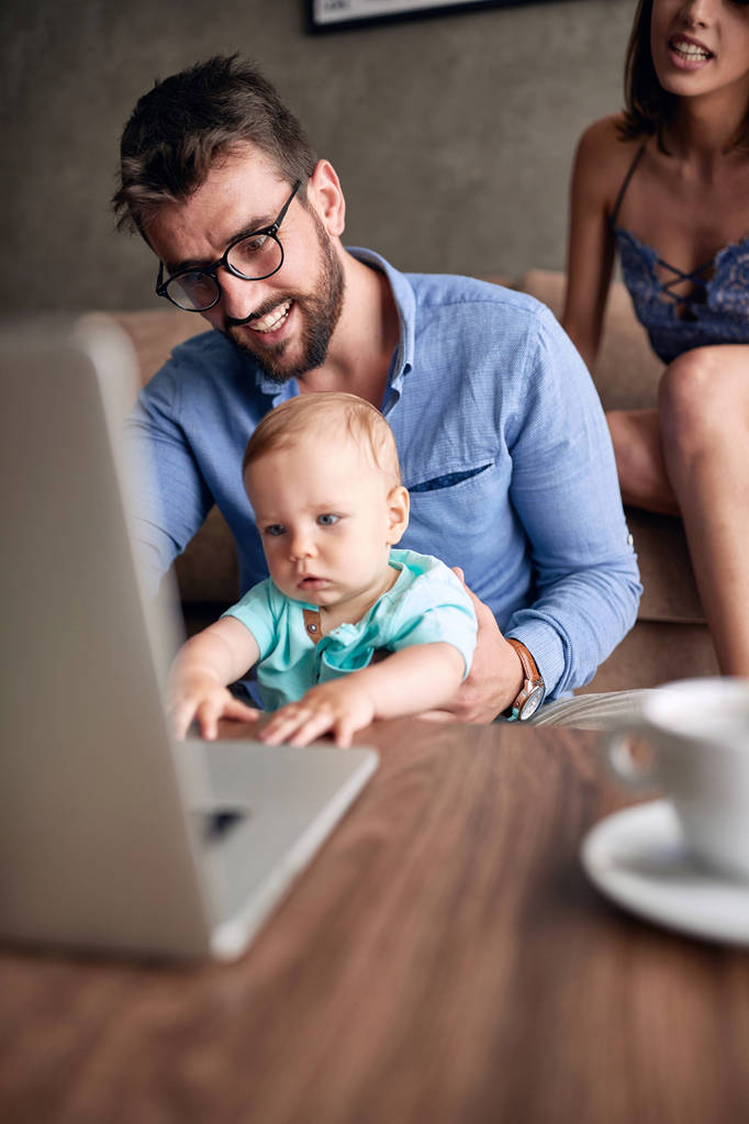 Sorridente padre occupato a lavorare con il computer mentre si prende cura del suo bambino figlio
 - Foto, immagini