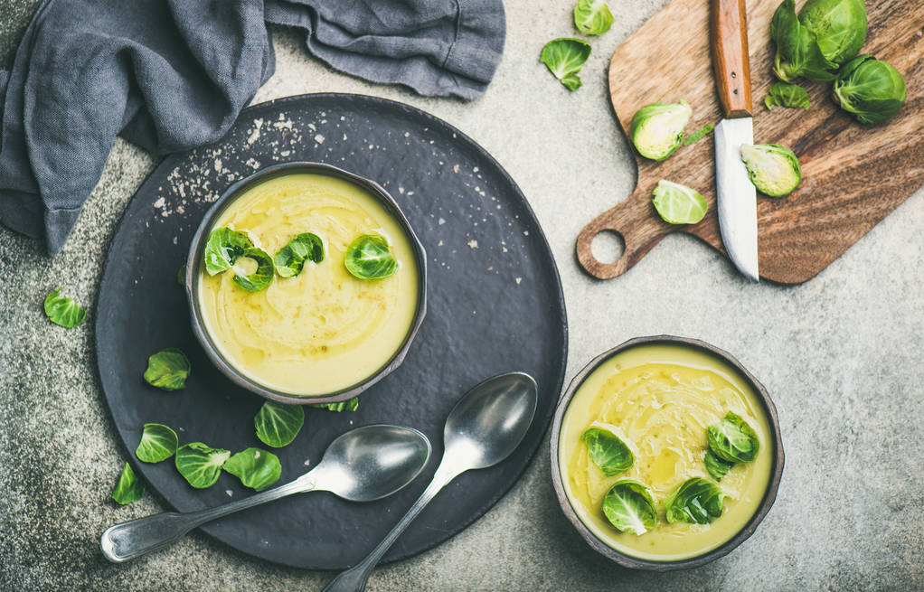 Soupe de légumes à la crème aux choux de Bruxelles de saison dans des bols noirs et choux de Bruxelles verts frais sur planche de bois
 - Photo, image