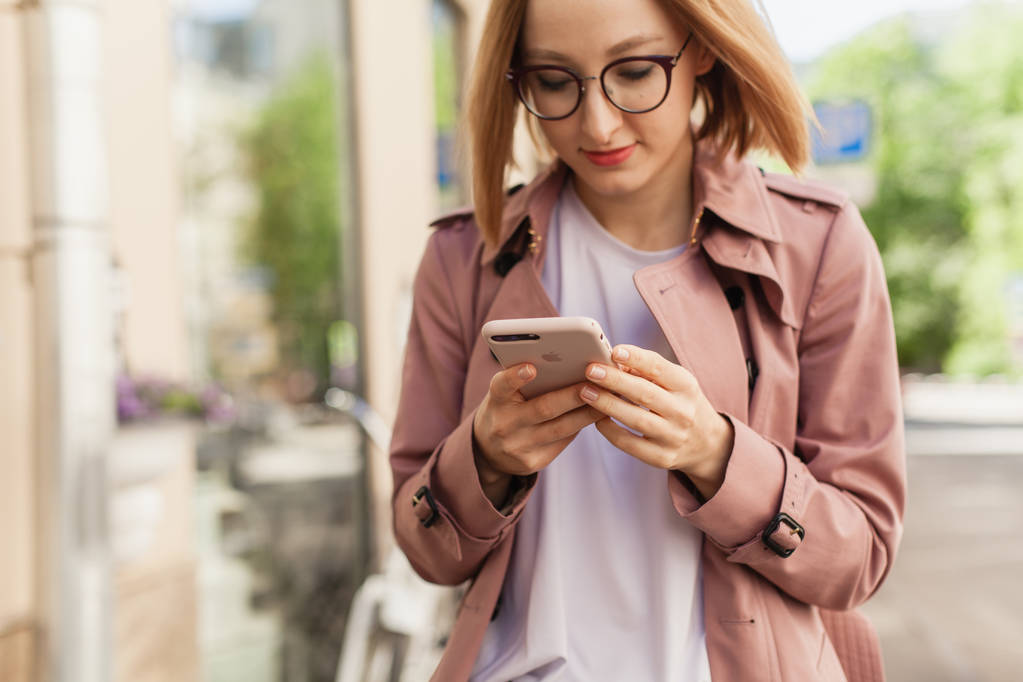 Onnellinen hymyilevä liikenainen modernilla älypuhelimella, menestyvä naisyrittäjä matkapuhelimen langattomalla yhteydellä kadulla, nuori nainen selaamassa matkapuhelinta ulkona
 - Valokuva, kuva