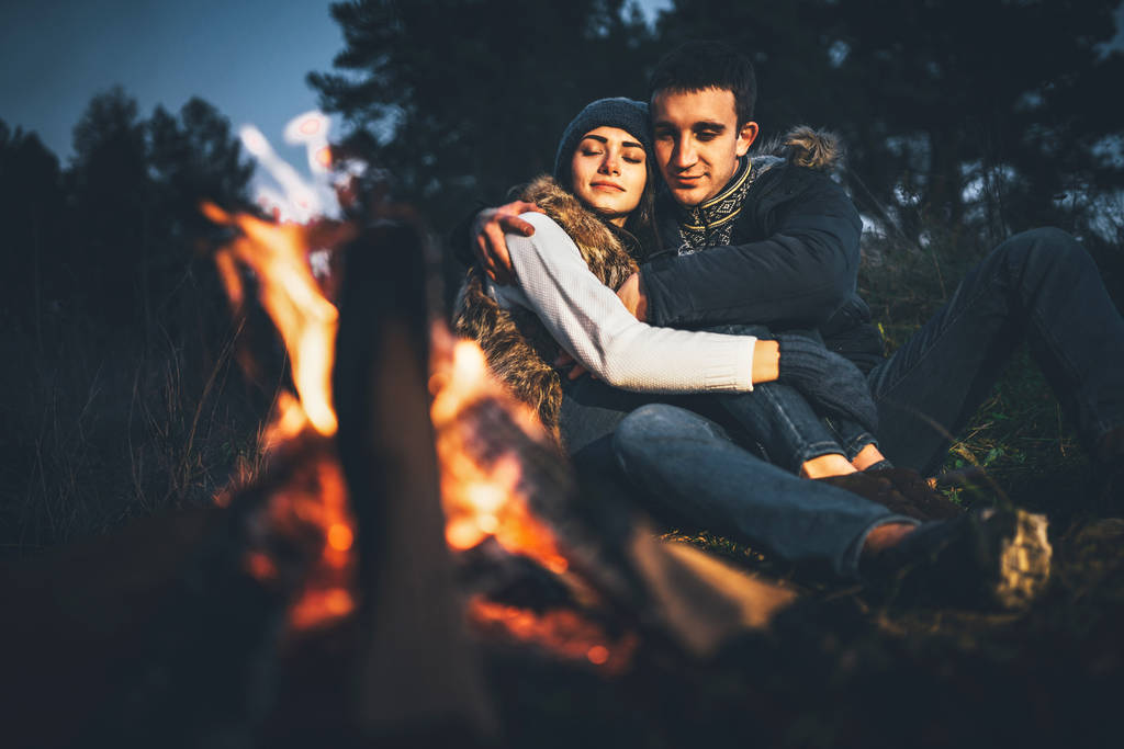 Χαλαρωτικό κοντά σε φωτιά στο δάσος ώρα το βράδυ αρκετά νεαρό ζευγάρι - Φωτογραφία, εικόνα