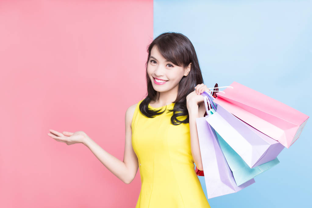 mulher com sacos de compras mostrando algo no fundo azul e rosa
 - Foto, Imagem