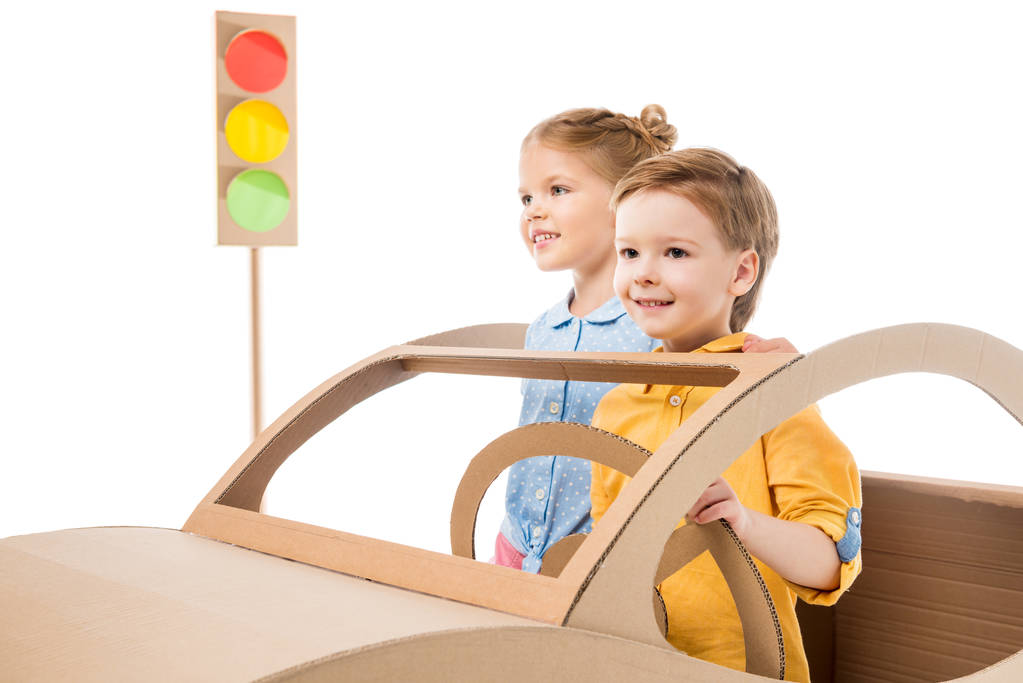 happy siblings playing with cardboard car and traffic lights, isolated on white  - Photo, Image