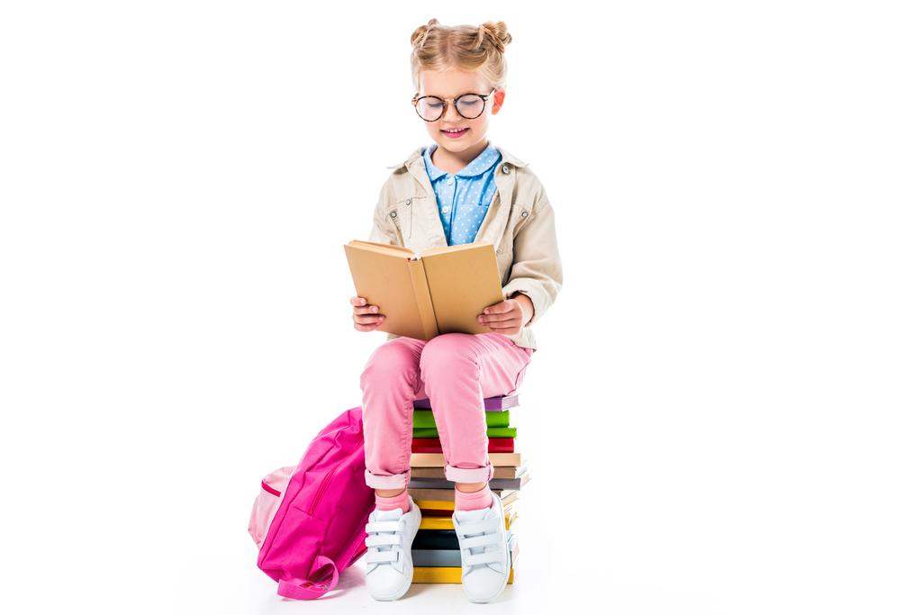 adorable écolière livre de lecture tout en étant assis sur une pile de livres avec sac à dos isolé sur blanc, concept d'éducation
 - Photo, image