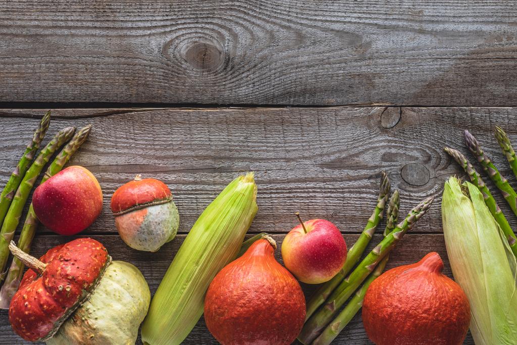 вид сверху на кукурузные початки, зеленую спаржу, тыквы и яблоки на сером деревянном столе
 - Фото, изображение