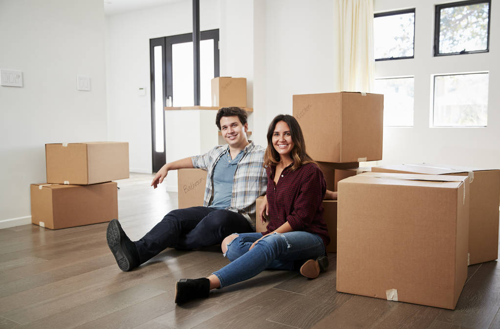 glückliches Paar sitzt am Umzugstag umgeben von Kisten im neuen Zuhause auf dem Boden - Foto, Bild