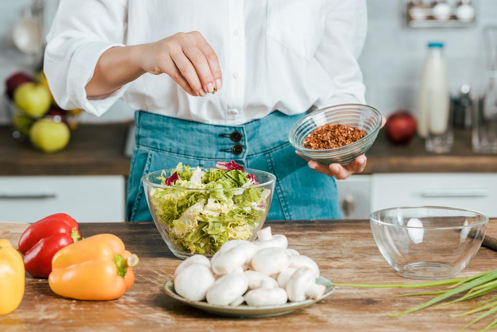oříznutý snímek žena rozsévá koření na salát v míse v kuchyni - Fotografie, Obrázek