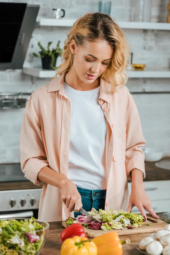 привлекательная молодая женщина режет салат для салата на кухне
 - Фото, изображение