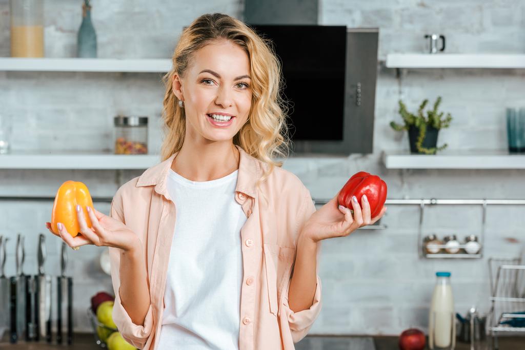 glückliche junge Frau mit reifen Paprikaschoten blickt in die Küche - Foto, Bild