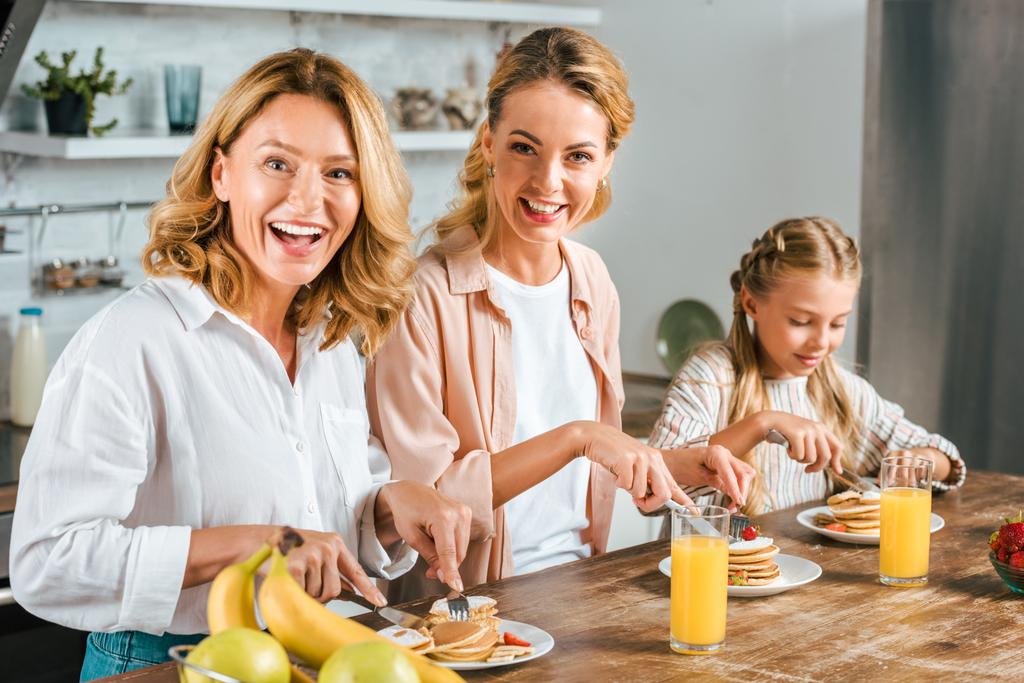 szczęśliwy trzy pokolenia kobiet o naleśniki na śniadanie w domu patrząc na kamery - Zdjęcie, obraz