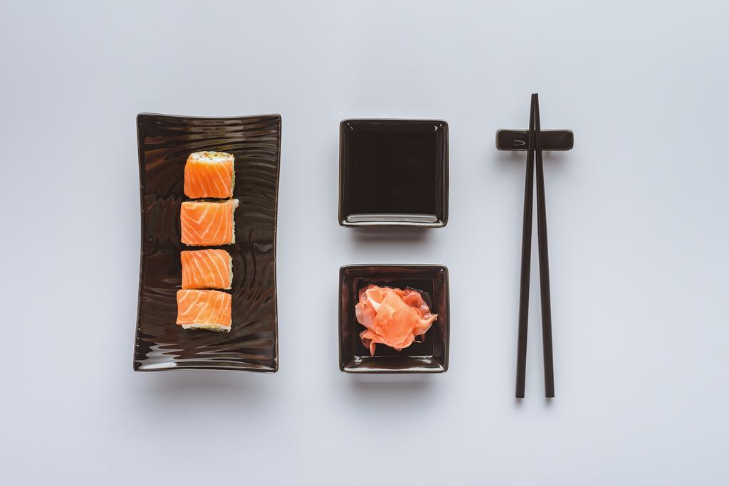 το Top view νόστιμο σούσι, με σολωμό, τζίντζερ, σάλτσα σόγιας και chopsticks απομονωθεί σε λευκό  - Φωτογραφία, εικόνα