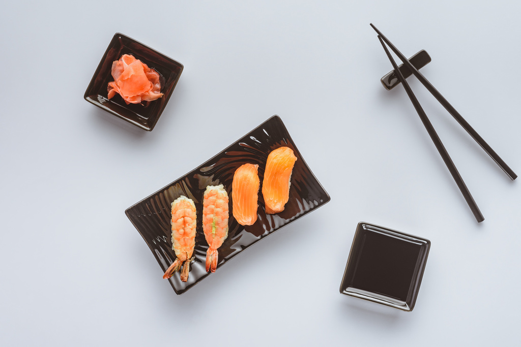 Draufsicht auf schmackhaftes Sushi mit Lachs und Garnelen, Ingwer und Essstäbchen isoliert auf weiß   - Foto, Bild