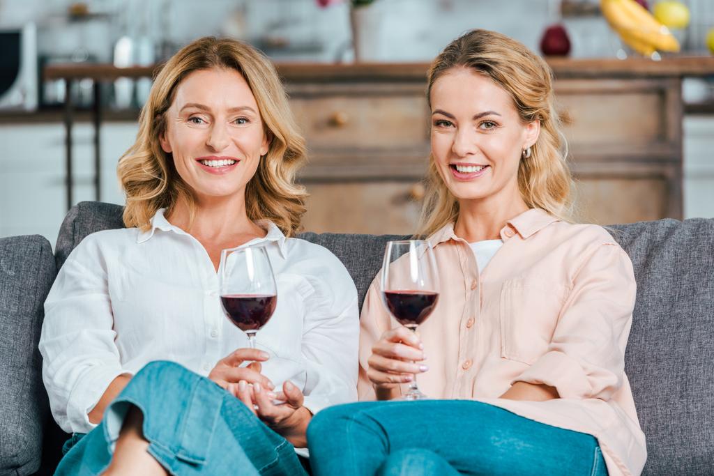 boldog, érett anya és felnőtt lánya pohár vörös bort tölteni az időt együtt otthon és látszó-on fényképezőgép - Fotó, kép
