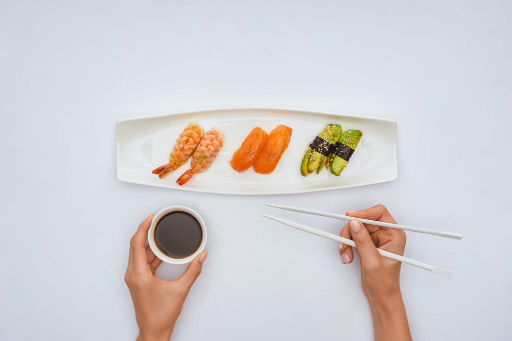 bijgesneden schot van houder van stokjes en kom met sojasaus terwijl het eten van sushi geïsoleerd op wit - Foto, afbeelding