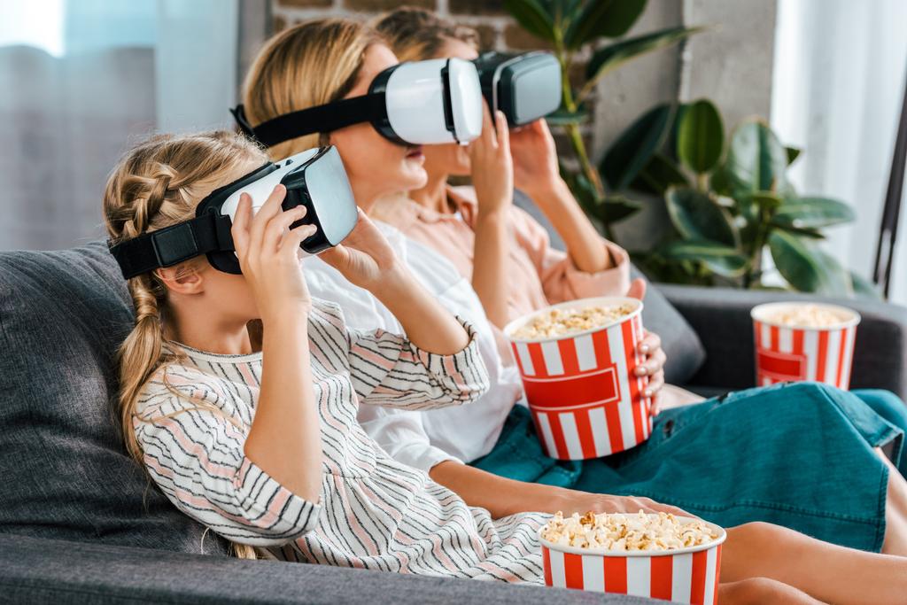 Zijaanzicht van kind met moeder en grootmoeder zit op de Bank samen en kijken naar film met virtuele realiteit headsets thuis - Foto, afbeelding